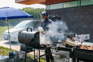man cooking at an outdoor grill with smoke rising up from the grill surface