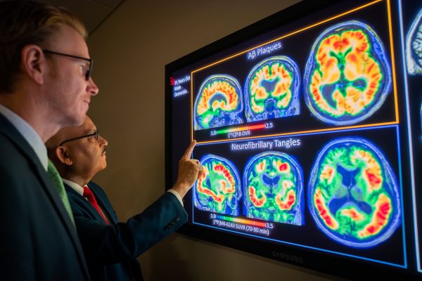two men in a dark room looking at a screen with PET scan images of a brain