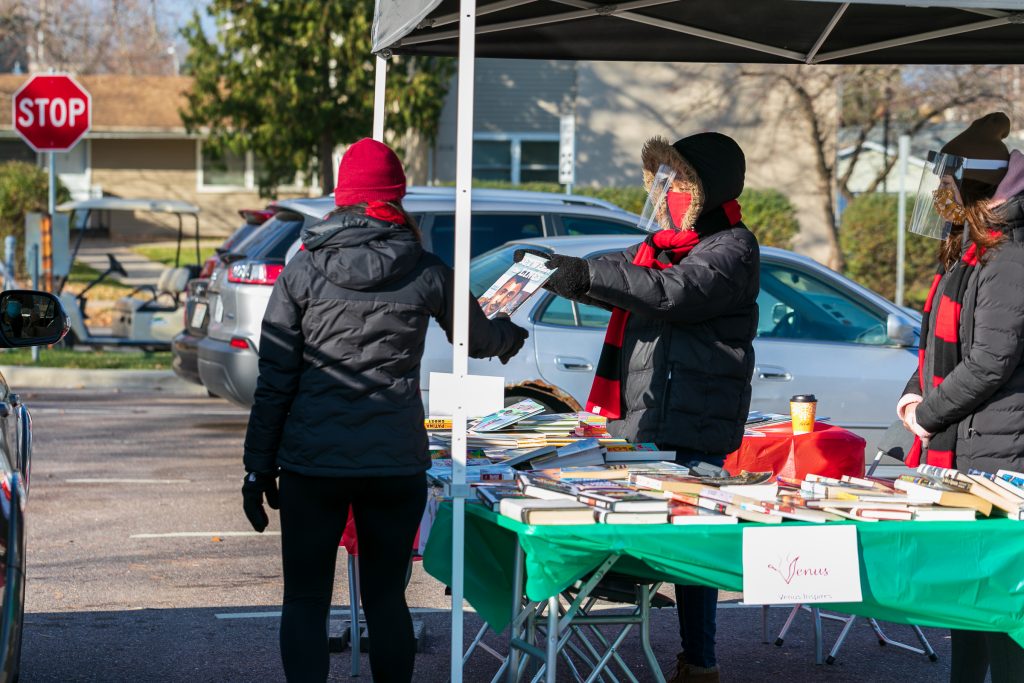 a person in a winter parka hands a book to another person during an outdoor event